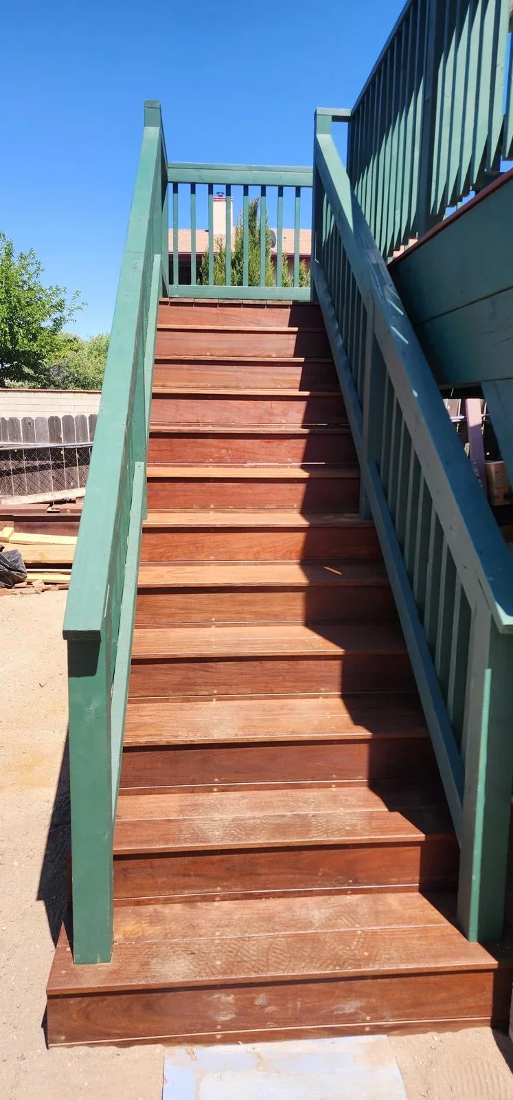 Wooden outdoor staircase with green metal railings and reddish-brown treads