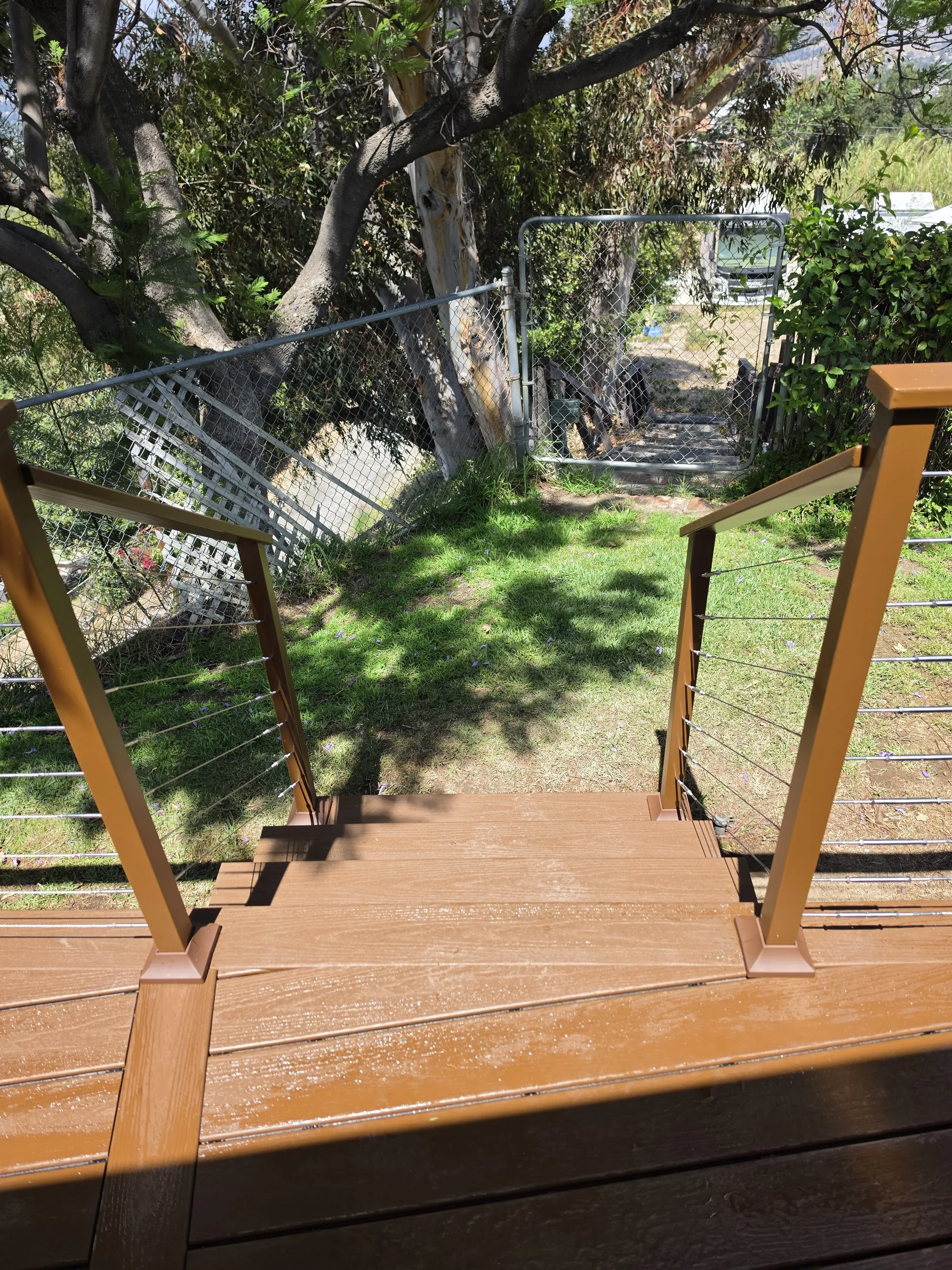 Composite deck with cable railing overlooking landscaped yard with mature trees