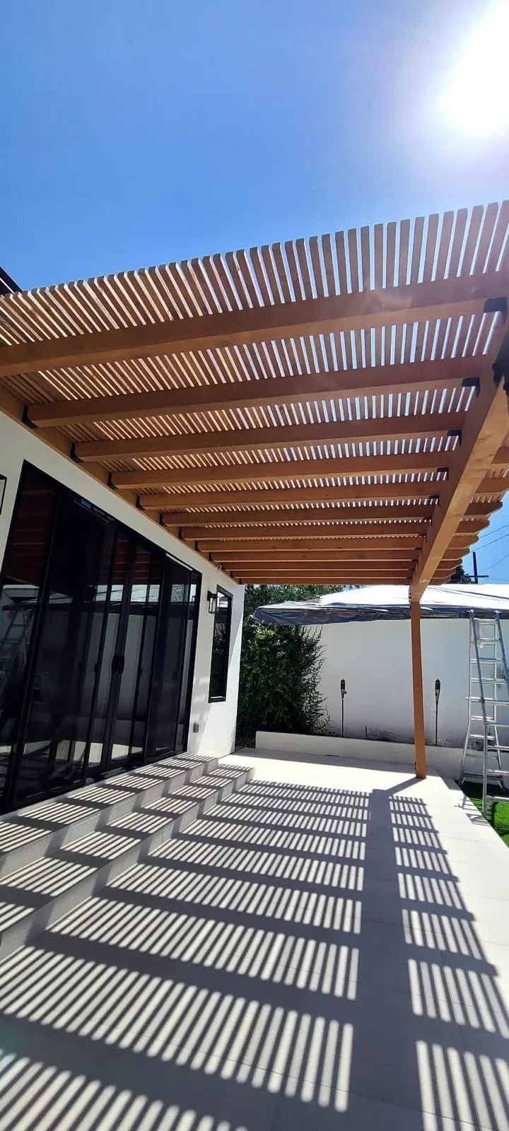 Wooden pergola with horizontal slats over concrete patio beside modern home