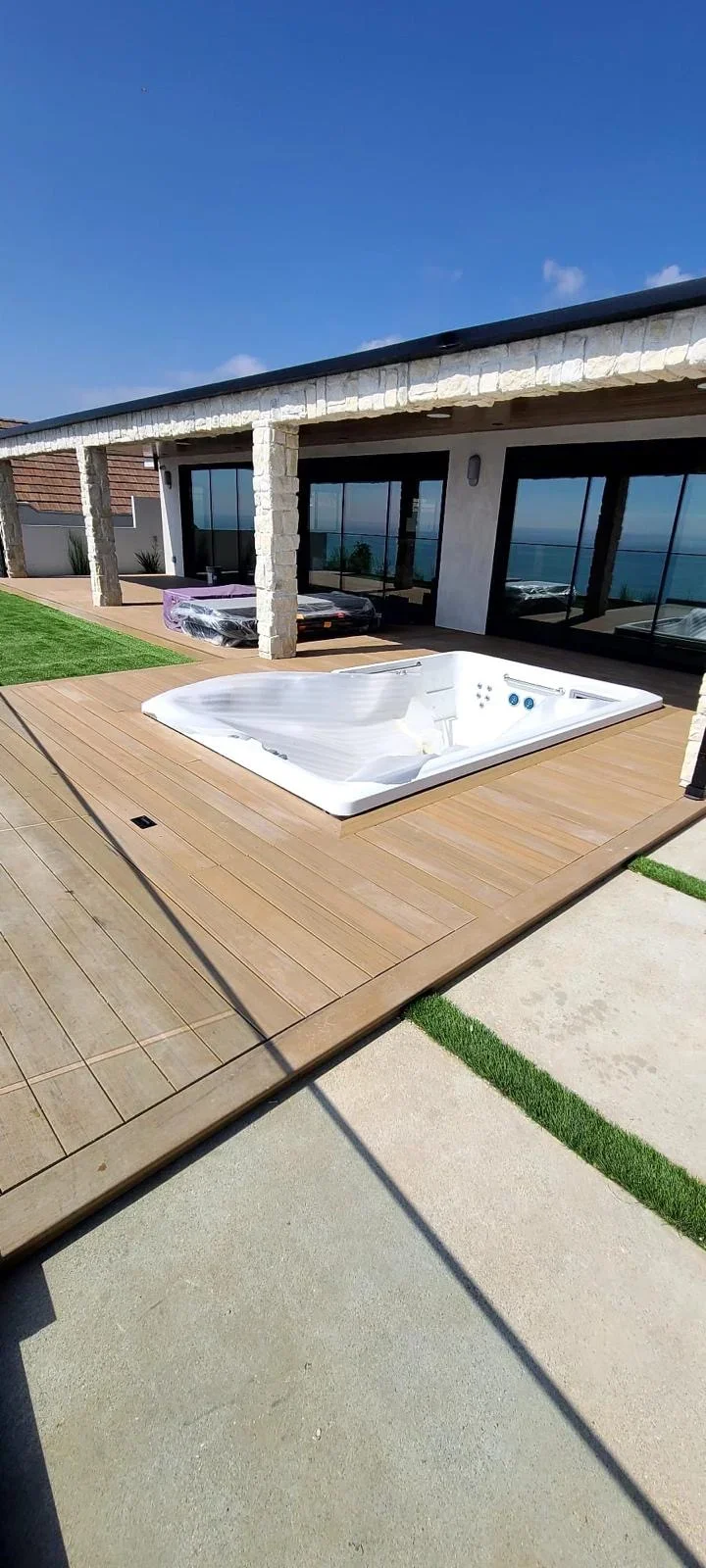 Composite deck with sunken hot tub overlooking ocean, modern home with glass doors