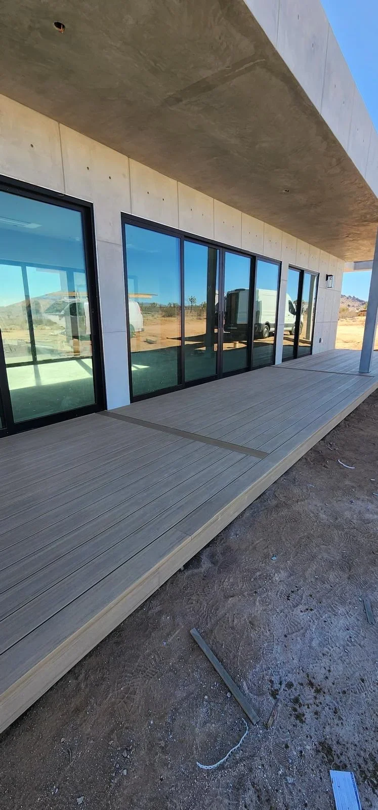 Gray composite deck with concrete soffit and black-framed glass doors overlooking desert landscape