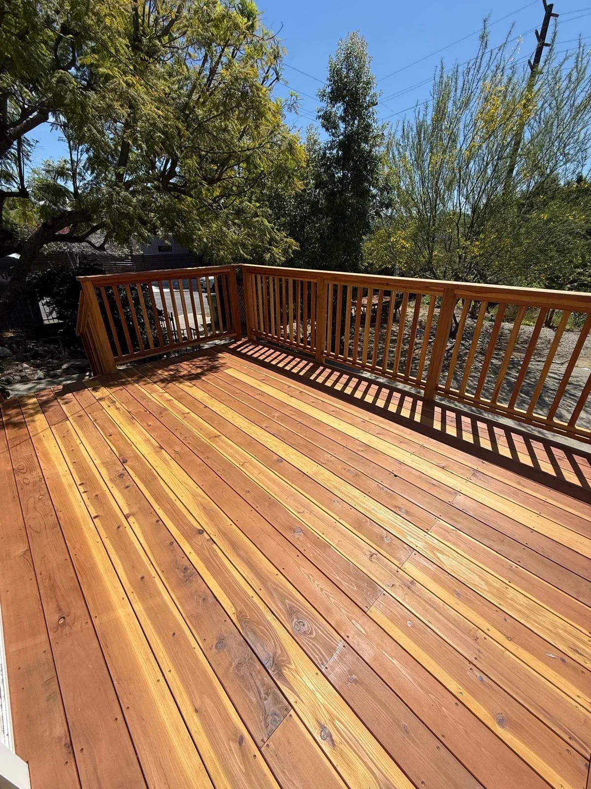 Large wood deck with stained boards and wooden railings overlooking landscaped yard
