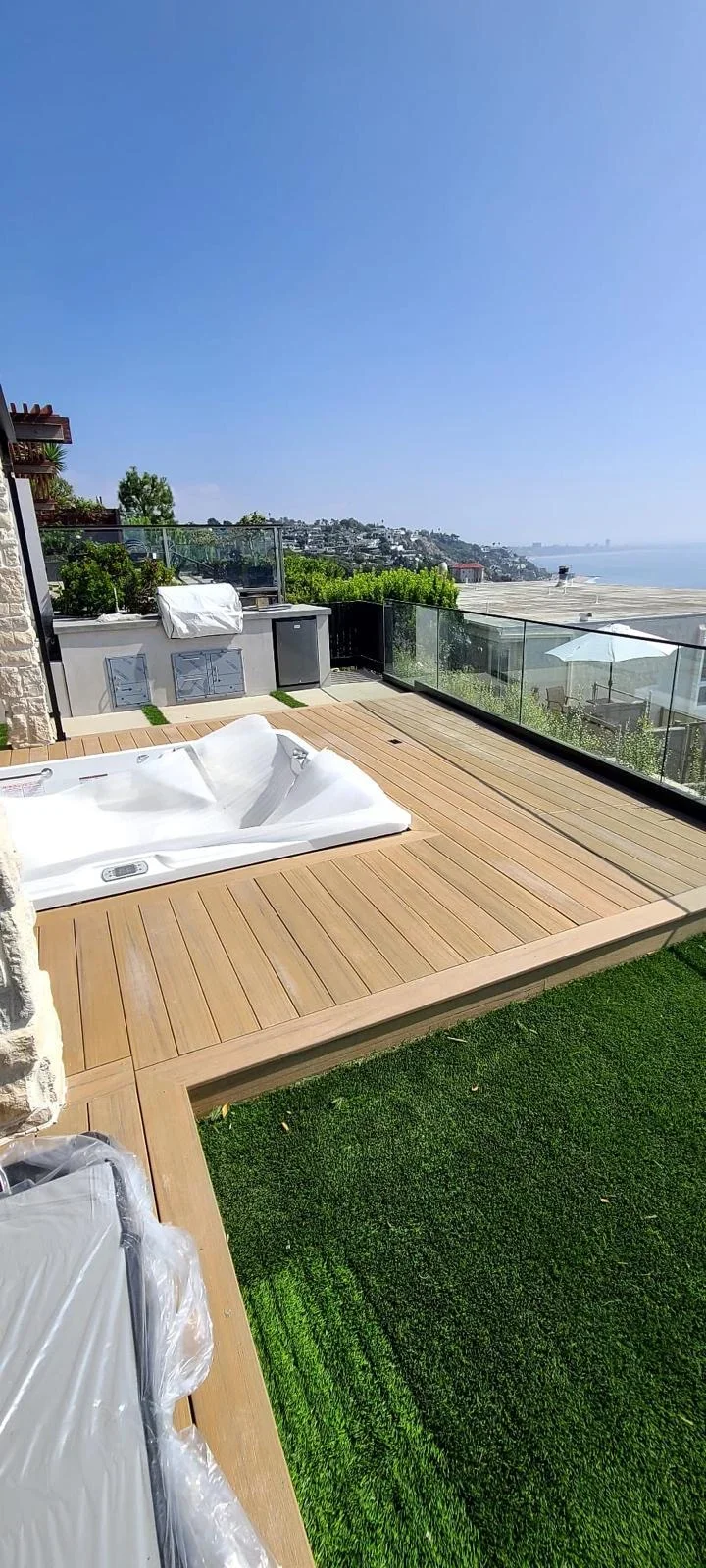 Composite deck with hot tub, glass railings, synthetic turf, and ocean view
