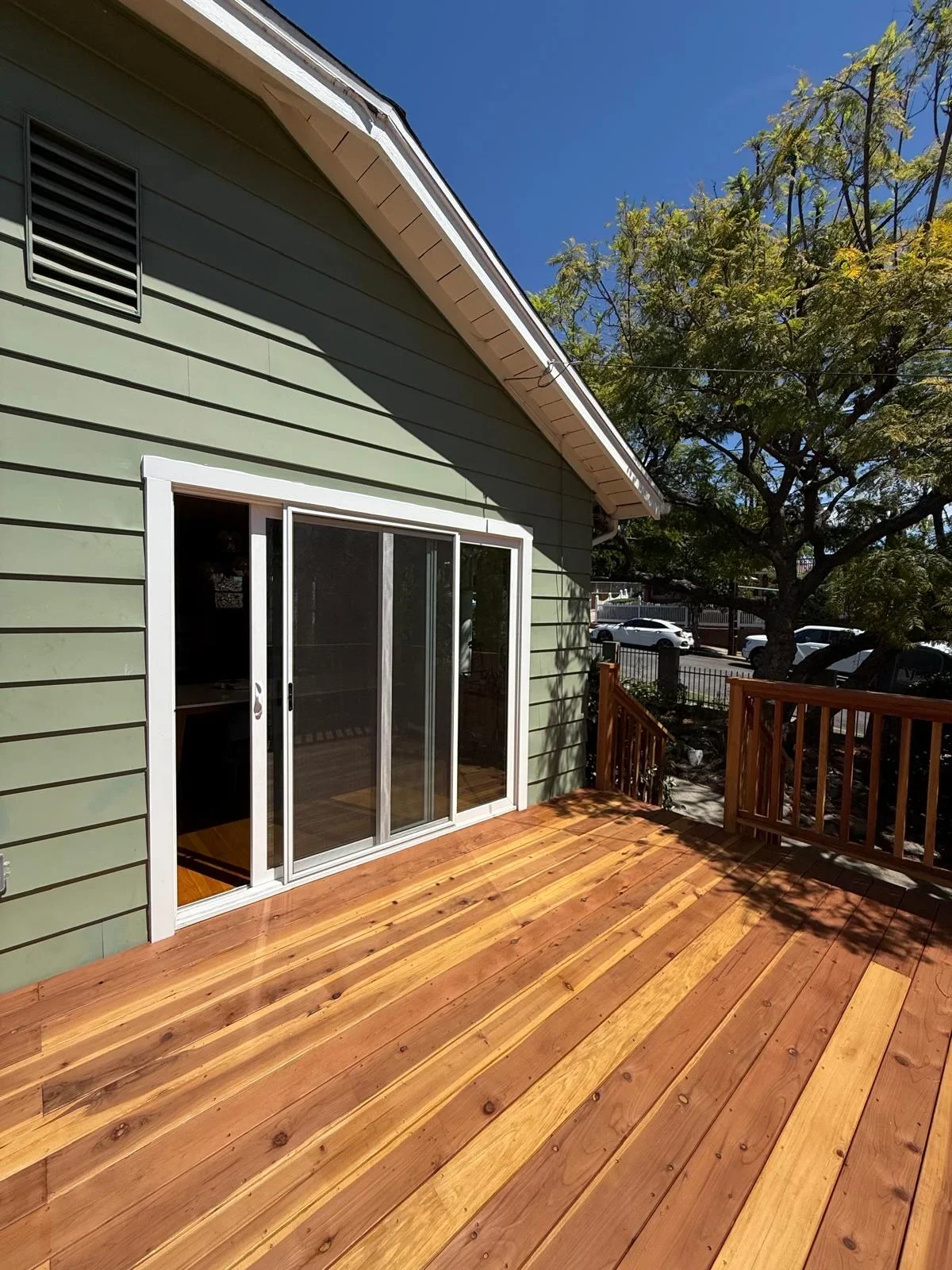 Newly built wooden deck with sliding glass doors and wooden railing on green house