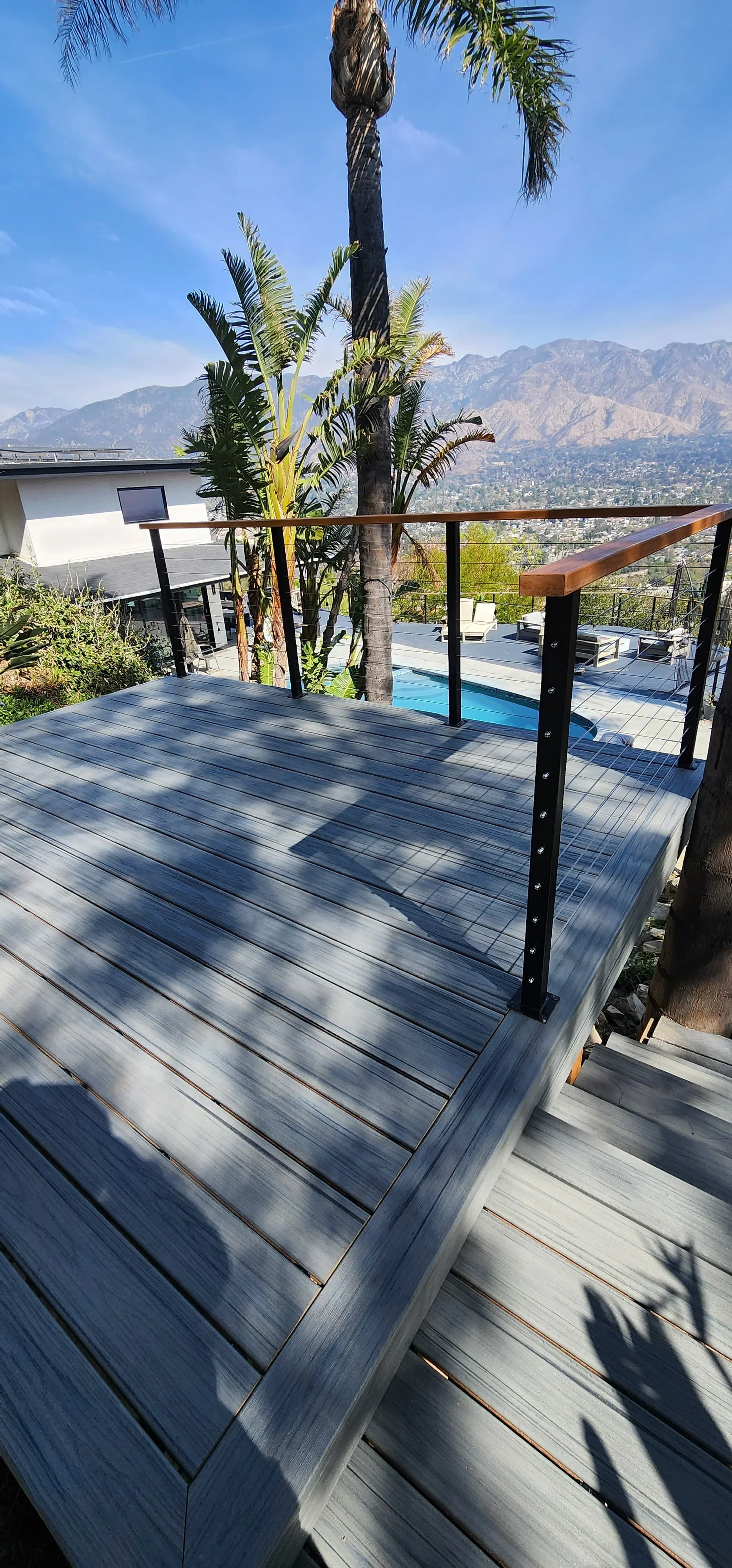 Gray composite deck with black metal railing overlooking pool and mountain views