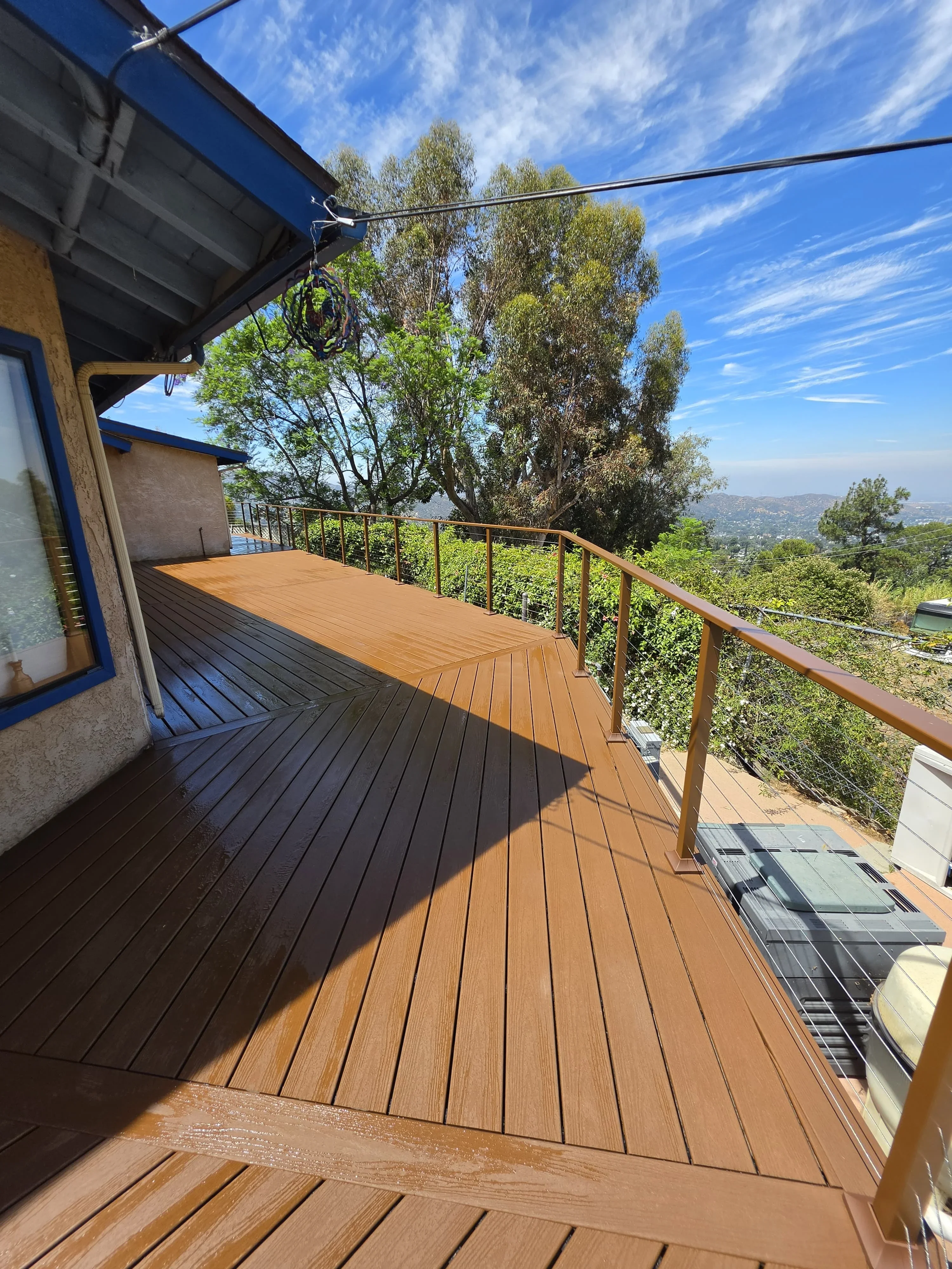 Composite deck with metal railing overlooking hillside landscape with mature trees