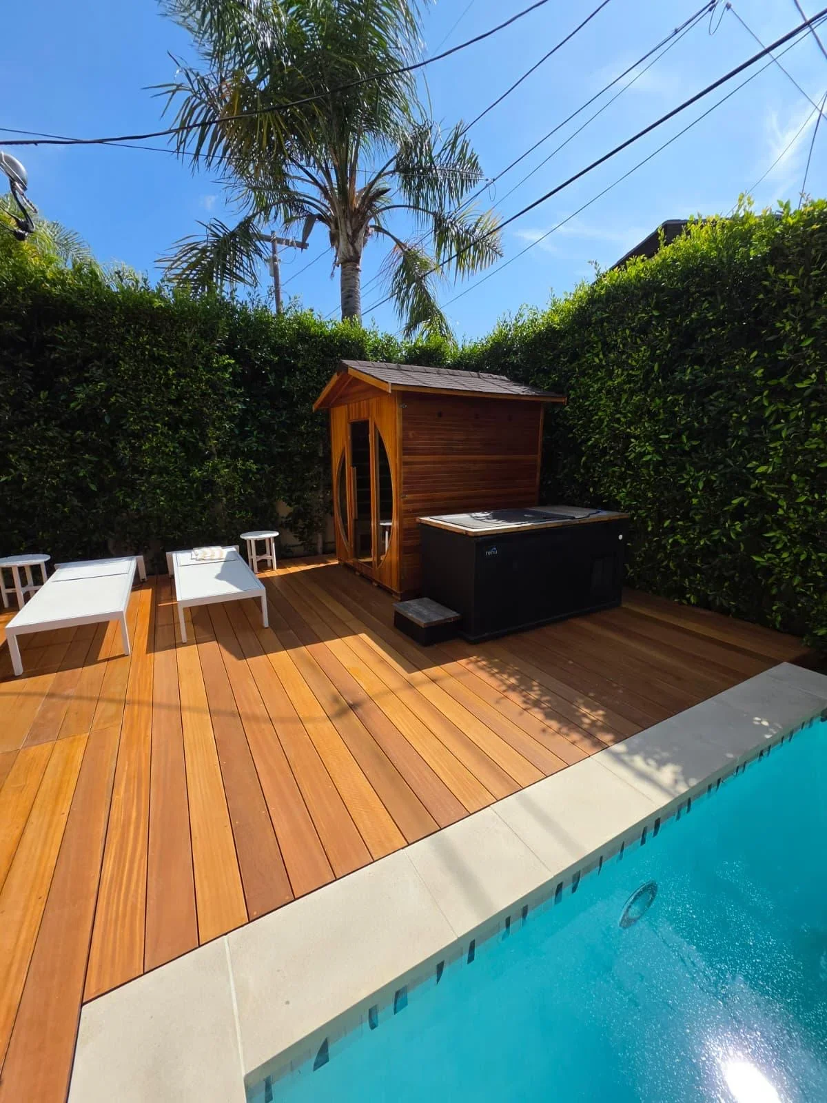 Wooden deck with hot tub, storage shed, and pool in tropical backyard setting